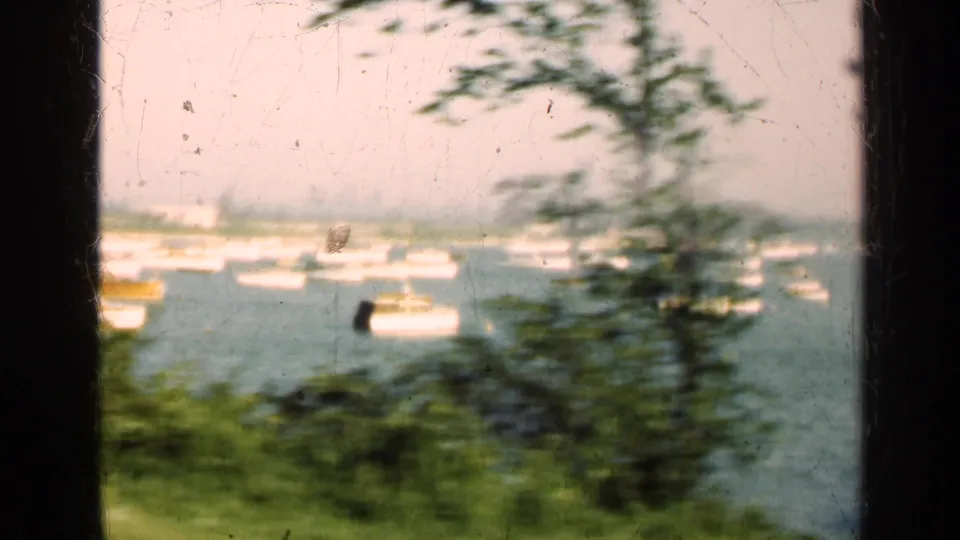 1947 Illinois 8mm frame with a vertical window bar, blurred trees, and multiple small boats on calm water.