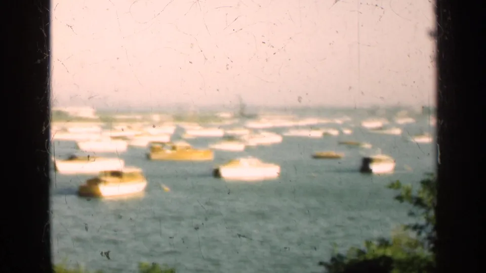 1947 Illinois 8mm frame showing clustered boats, including a yellow vessel, viewed across water from behind a dark window edge.