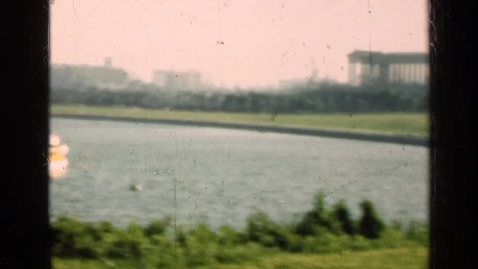 1947 Illinois 8mm frame looking across water toward a distant urban shoreline and large building, framed by dark window bars.