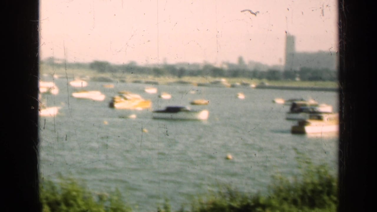Soft 8mm frame of boats on an Illinois lake in 1947, with bright water, distant trees, buildings, and a tower in the background.