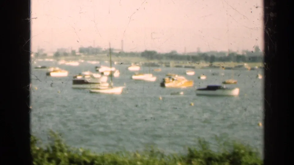 1947 Illinois lakeside view with anchored boats, green foreground vegetation, distant buildings, and a dark window-frame division.