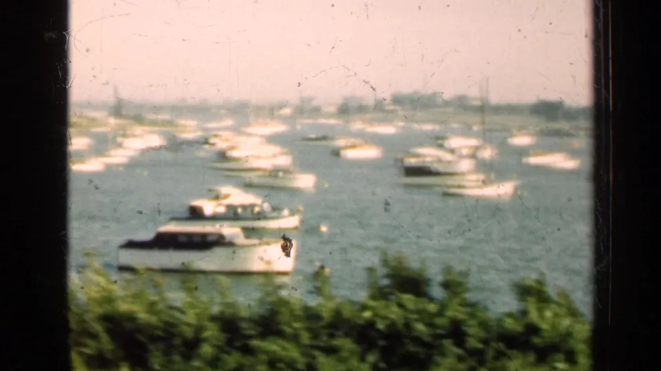 Soft 1947 Illinois 8mm frame showing a white cabin boat near the foreground, scattered boats, greenery, and a hazy shoreline.