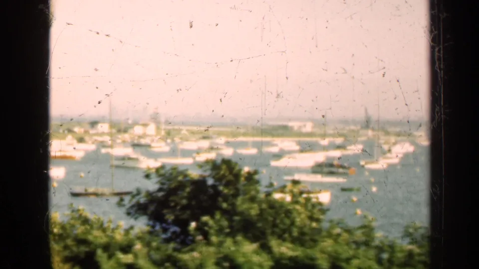 1947 home-movie harbor view in Illinois with boats at anchor, leafy foreground, distant shoreline, and visible 8mm wear.
