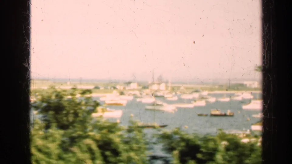 Soft 1947 Illinois 8mm frame of harbor boats, low shoreline structures, greenery, and dark window or gate edge.