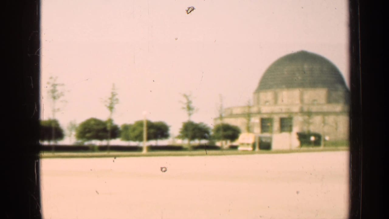 Domed building seen beyond dark vertical window frames and an open paved area.