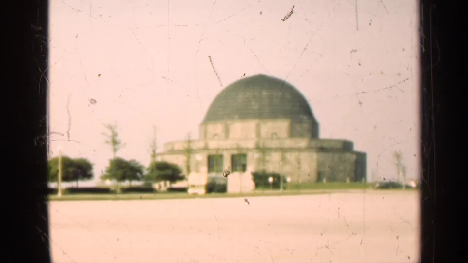 1947 Illinois 8mm frame of a large domed building with small trees and vehicles along the front edge of an open lot.