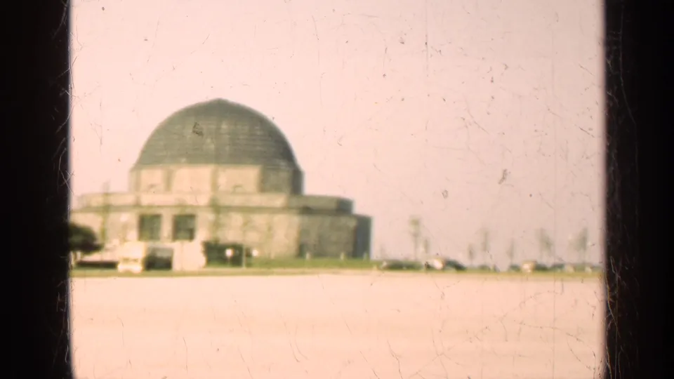Soft 8mm frame from 1947 Illinois showing the domed building cropped low and left across a bright paved foreground.
