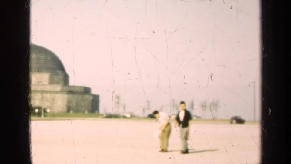 1947 Illinois home-movie frame with two men crossing the paved lot while the domed building remains in the background.
