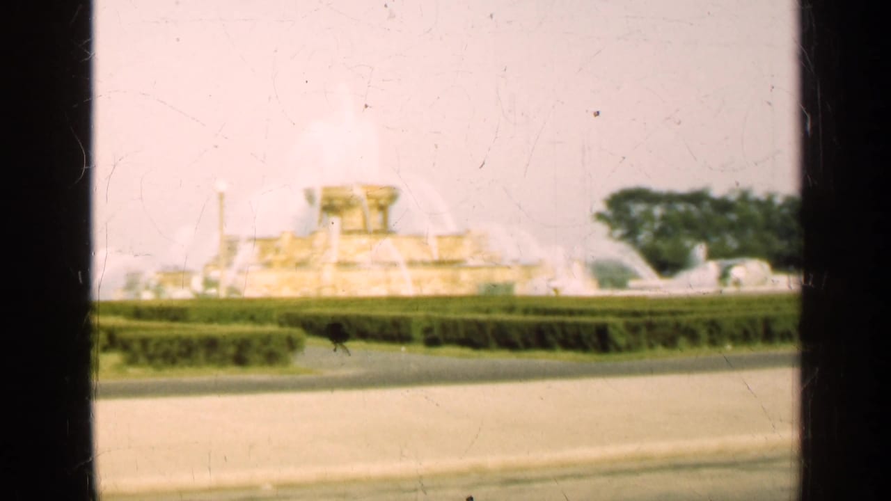 Large fountain centered behind low hedges with arcing water jets and trees nearby.