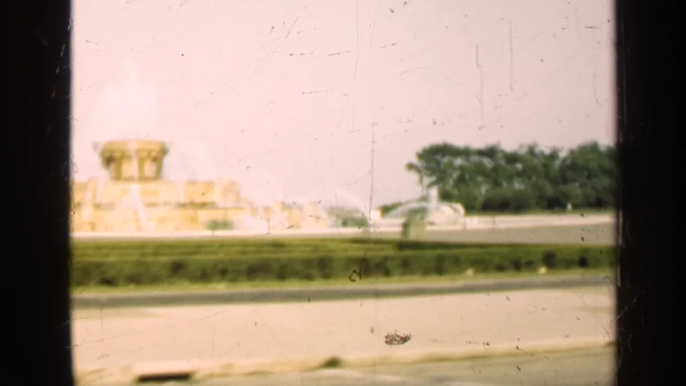 1947 Illinois frame of a sunlit fountain and formal landscaping, bordered by dark 8mm gate edges and surface dust.