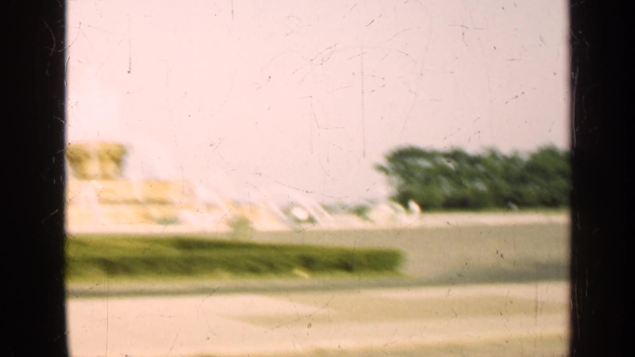 1947 Illinois home-movie frame showing a soft distant fountain across a lawn, partly blocked by dark window dividers.