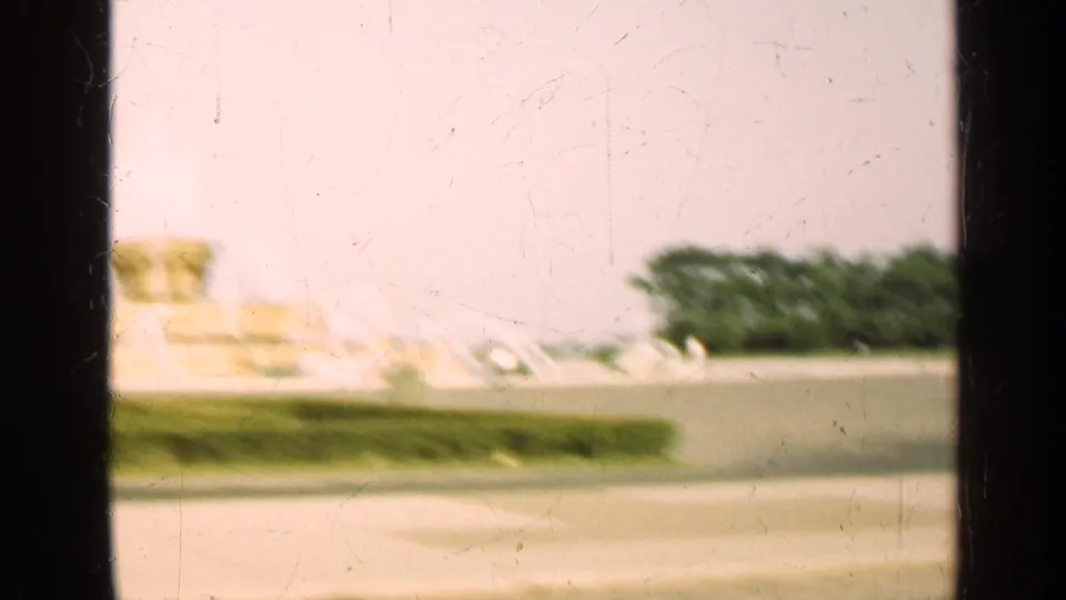 1947 Illinois home-movie frame showing a soft distant fountain across a lawn, partly blocked by dark window dividers.
