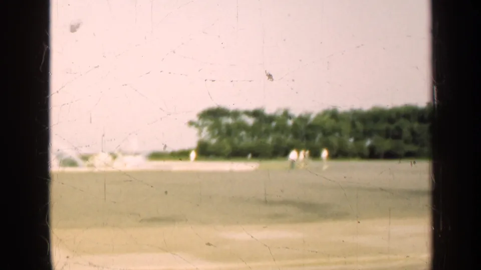 1947 Illinois 8mm frame of an open park lawn, distant trees, and several small walkers seen from a windowed viewpoint.
