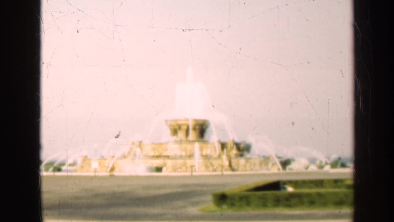 Large fountain spraying water beyond a road and lawn, partly divided by dark frame edges.