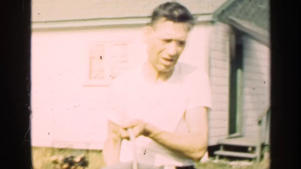 The man is seen closer to camera holding or handling a bucket outside the Illinois house in bright 8mm footage.