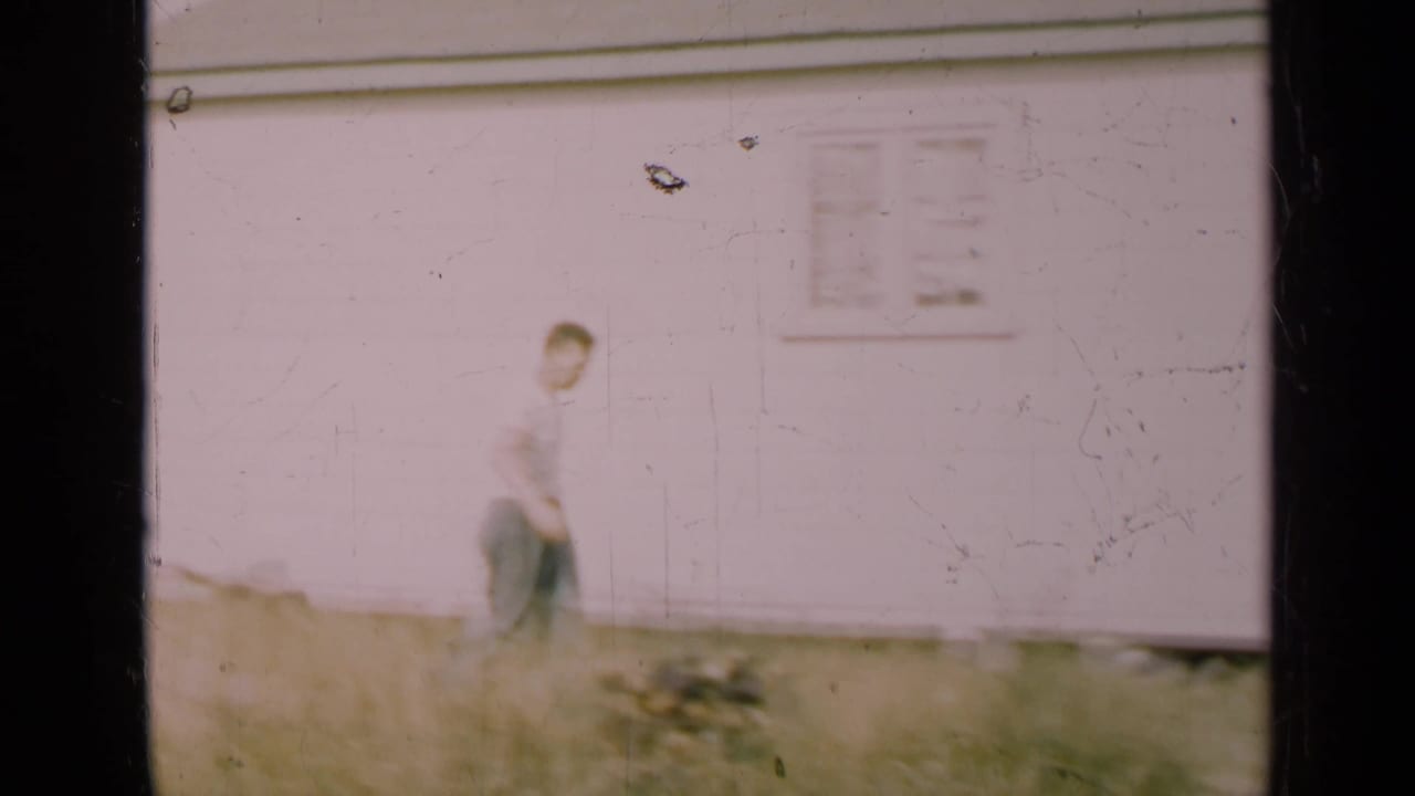 Man walking near the white house wall through tall grass.