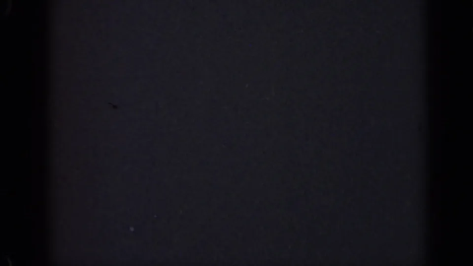 Underexposed 1947 Illinois 8mm home-movie frame showing mostly darkness with faint bluish film grain and tiny surface specks.