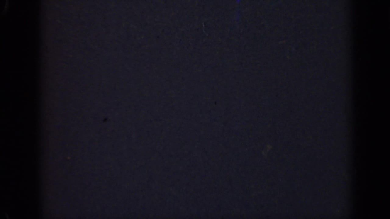 Dark 1947 Illinois 8mm home-movie frame with little visible subject detail beyond grain, vertical banding, and scattered dust specks.