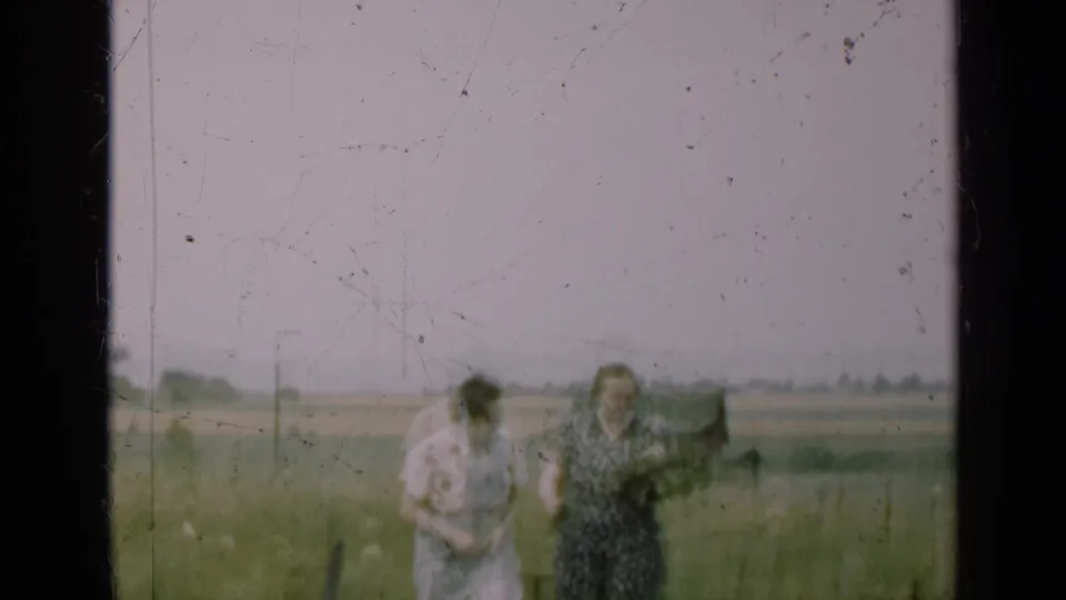 Two women in mid-century dresses move through a grassy Illinois field in soft 8mm footage from the supplied 1947 setting.