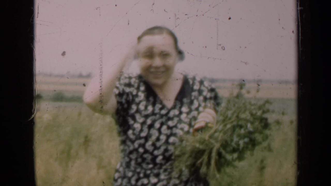A woman in a patterned dress holds a bundle of green plants and smiles toward the camera in a rural Illinois field.
