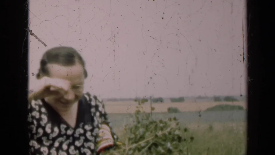 In a soft 8mm frame, the woman shields her eyes from light while standing with gathered plants in an Illinois field.