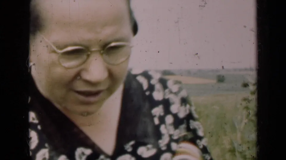 Close 1947 Illinois home-movie view of the woman wearing glasses, leaning toward the camera with farmland behind her.
