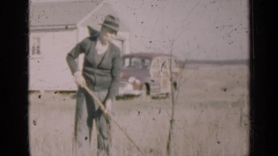 The closing frame keeps the man hoeing in a rural Illinois yard, with farmhouse wall and vintage car behind him.