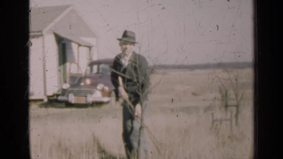 The 1947 Illinois footage shows the man facing the camera while working in open grassland near a white house and parked mid-century car.
