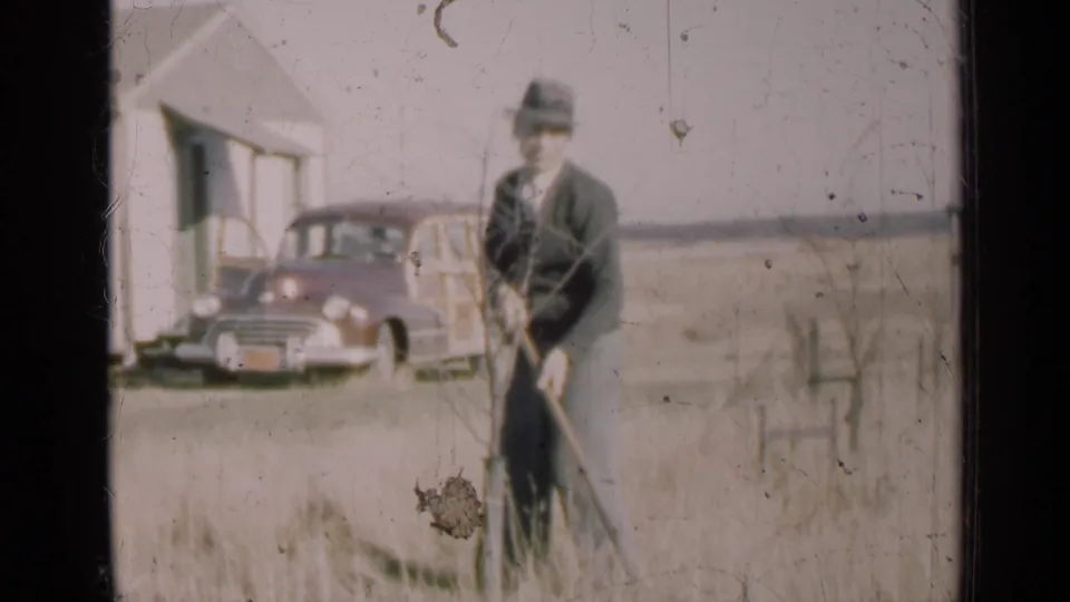 A man in 1947 Illinois appears to tend a sapling in tall grass, framed by a white rural house and a parked 1940s automobile.
