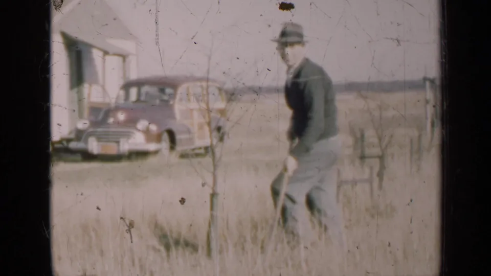 The final frame shows the man turned sideways while tending the ground near a sapling in rural Illinois, with the house and car still visible.
