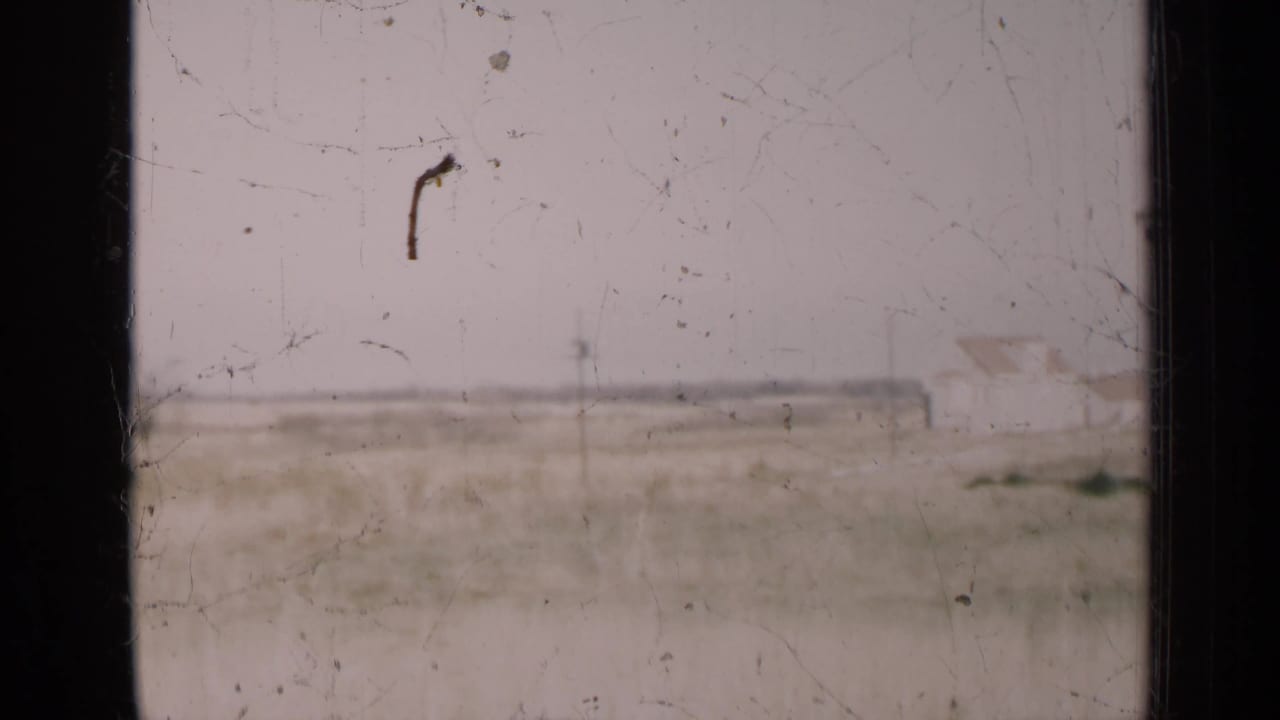 Soft 8mm frame of an open Illinois field with pale sky, horizon line, and visible film wear.