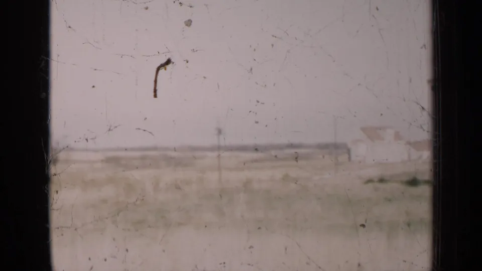 Soft 8mm frame of an open Illinois field with pale sky, horizon line, and visible film wear.