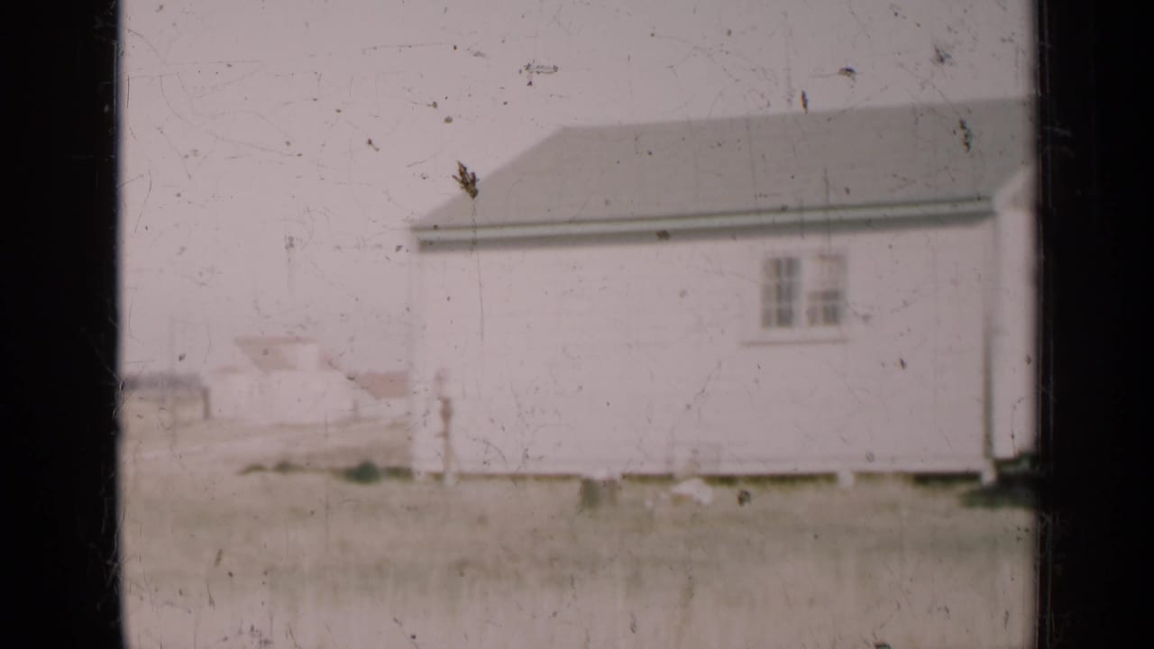 1947 Illinois 8mm frame showing a white rural building across a flat field, with no people visible.
