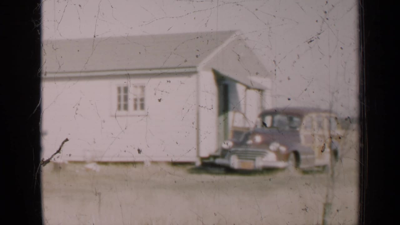 Wood-paneled station wagon parked beside a white rural building.