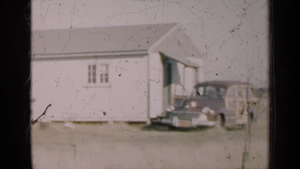 1947 Illinois home-movie frame with a wood-sided station wagon parked near a white rural building.