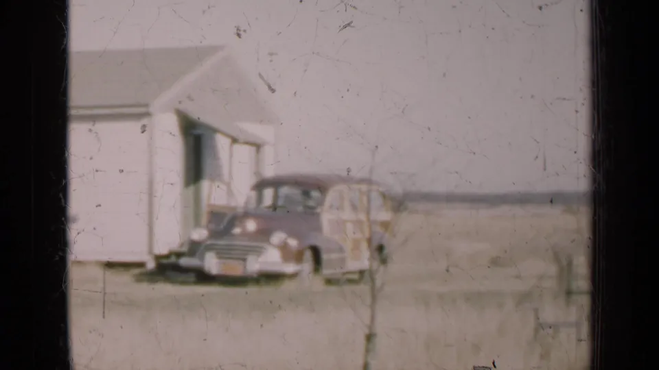 1947 Illinois frame showing the parked station wagon closer to the building corner, with open land behind it.