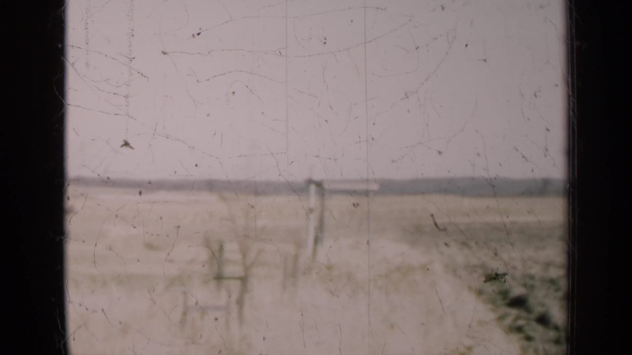 Flat rural field and distant utility poles seen through a dark window frame.