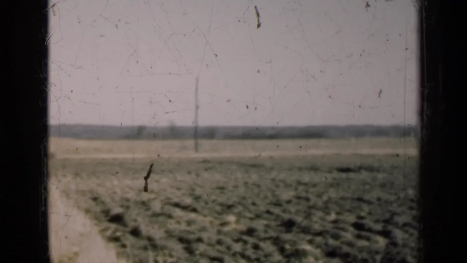 Weathered 8mm view of an Illinois field in 1947, with plowed ground, distant utility poles, and dark window framing in the foreground.