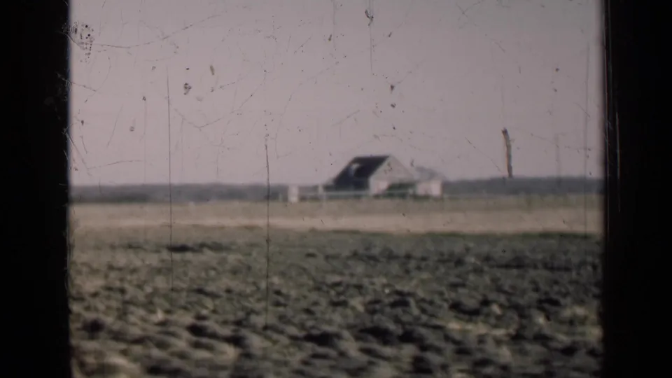 1947 Illinois 8mm frame showing an open rural field with a distant farm building under a pale sky.