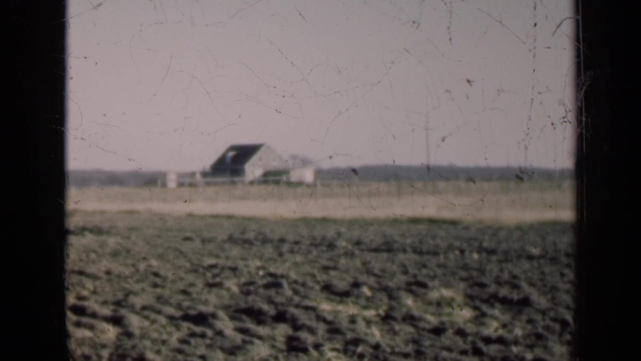 Open field and distant low building seen through dark vertical film borders.