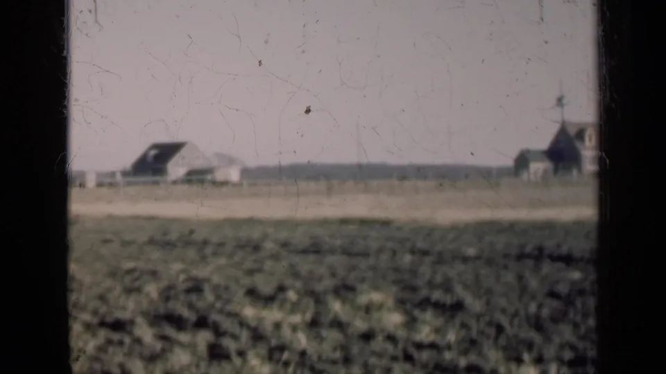 1947 Illinois 8mm frame showing open field and distant rural structures, one with a steeple-like roofline.