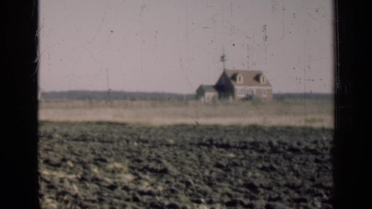 1947 Illinois 8mm frame showing a distant rural farmhouse beyond a field, partly framed by a dark window edge.