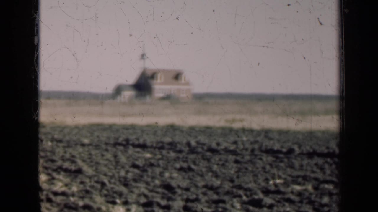 Soft 8mm view of a rural Illinois farmhouse across open fields, with a dark window divider cutting through the frame.