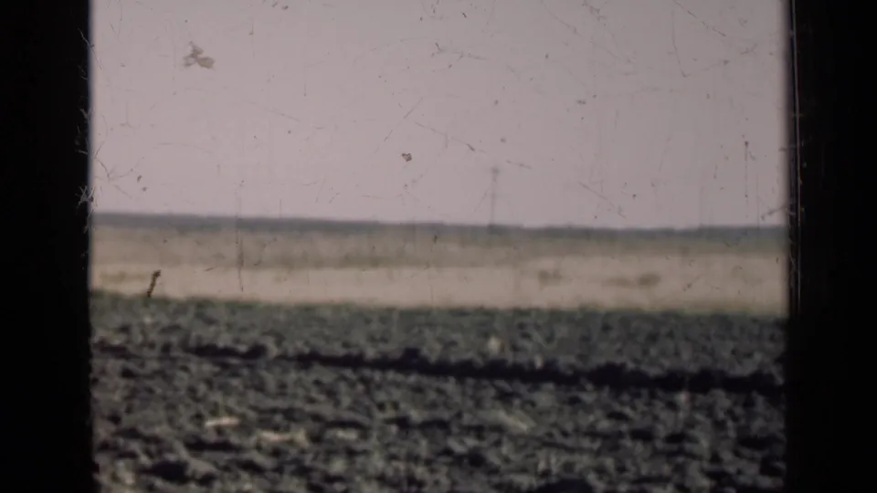 Final 8mm frame shows mostly open Illinois field and horizon through the vehicle window after the farmhouse has nearly passed from view.