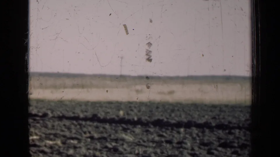 1947 Illinois farmland with a plowed foreground, pale sky, flat horizon, and dark window-frame bars crossing the view.