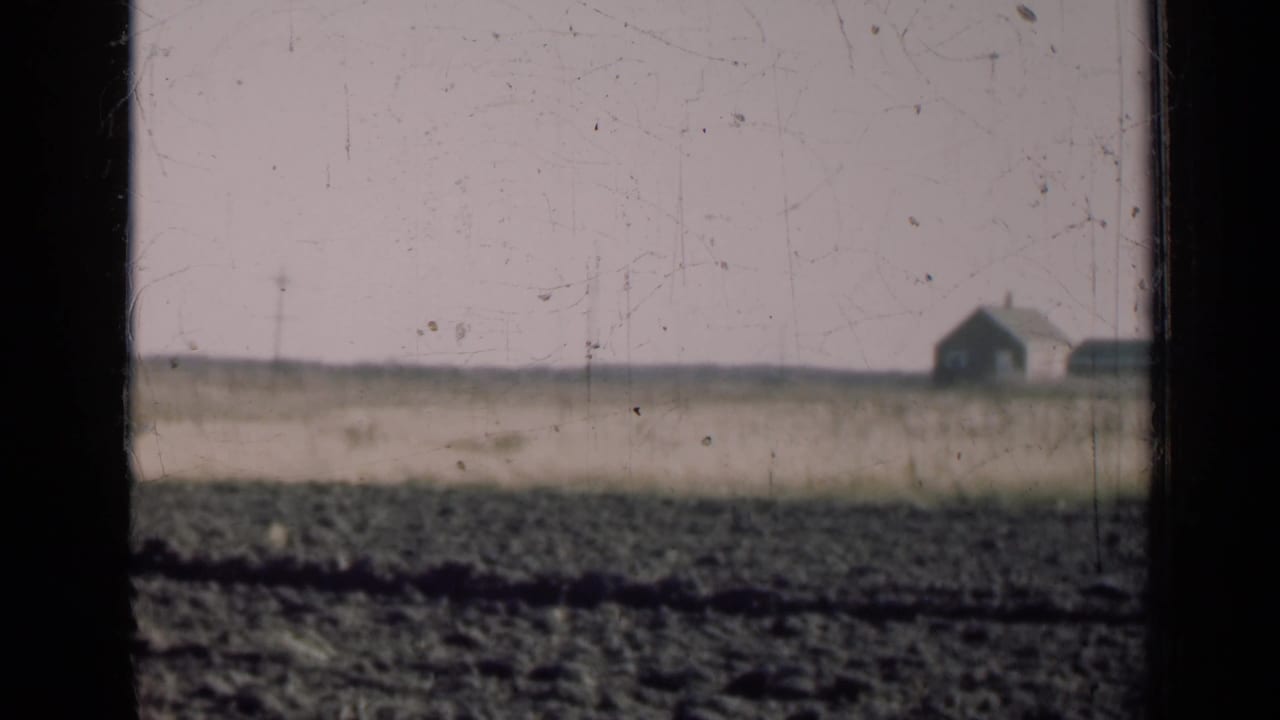 A small farmhouse appears in the far distance across an Illinois farm field, partly framed by dark vertical bars.