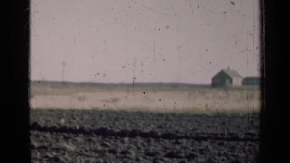 A small farmhouse appears in the far distance across an Illinois farm field, partly framed by dark vertical bars.