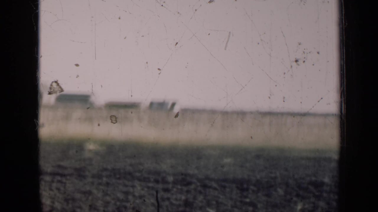 1947 Illinois farmland appears beyond a dark window frame, with plowed fields and a pale sky softened by aged 8mm film texture.