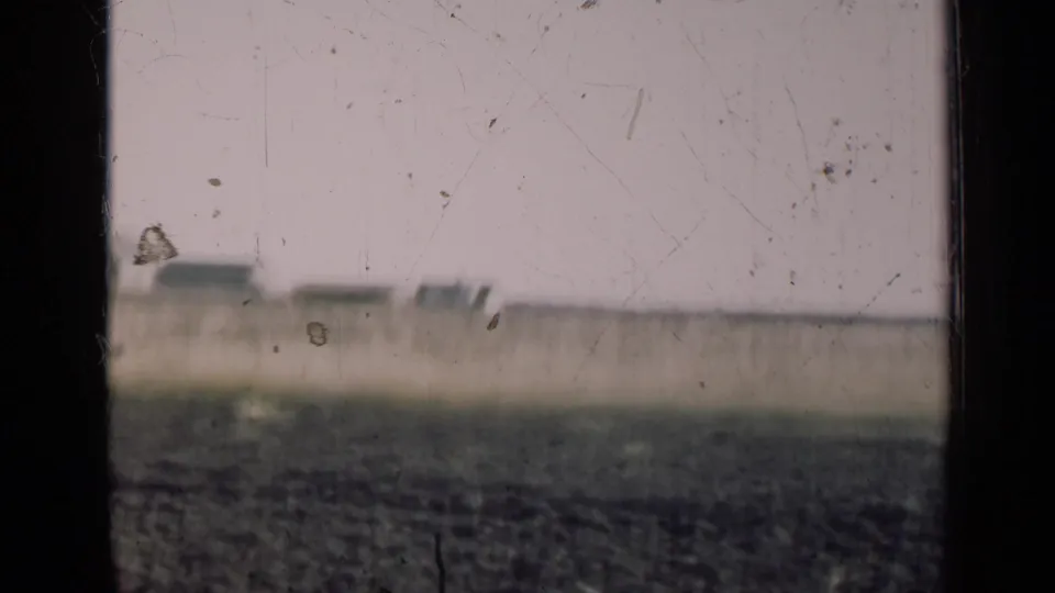 1947 Illinois farmland appears beyond a dark window frame, with plowed fields and a pale sky softened by aged 8mm film texture.