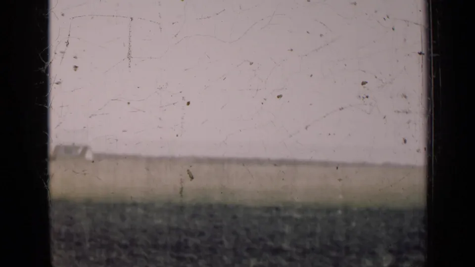 A flat Illinois field and low horizon sit behind a central dark frame bar, with visible scratches and grain from the 8mm source.
